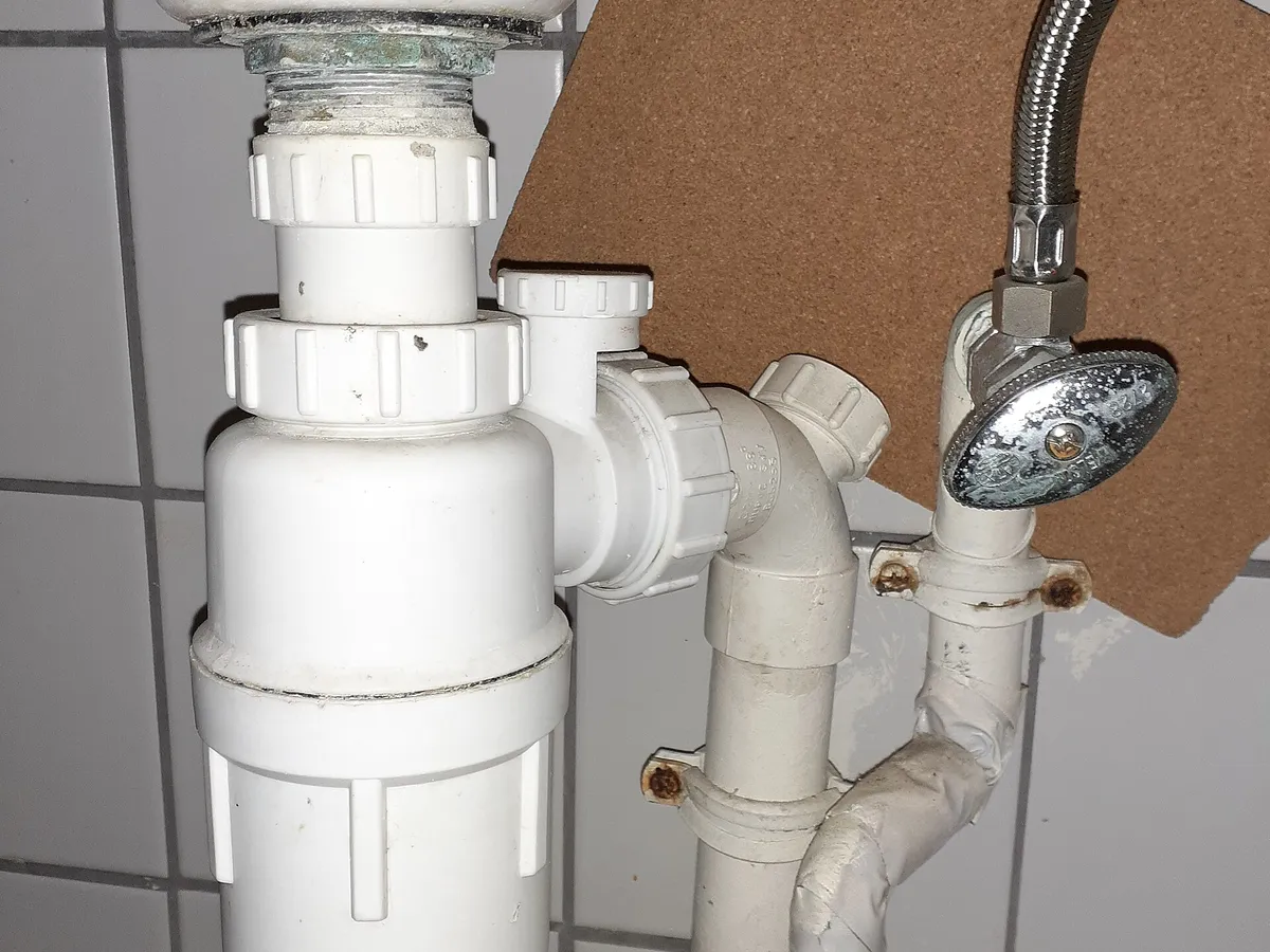 White plastic bottle trap and drain pipes under a wall-hung sink
