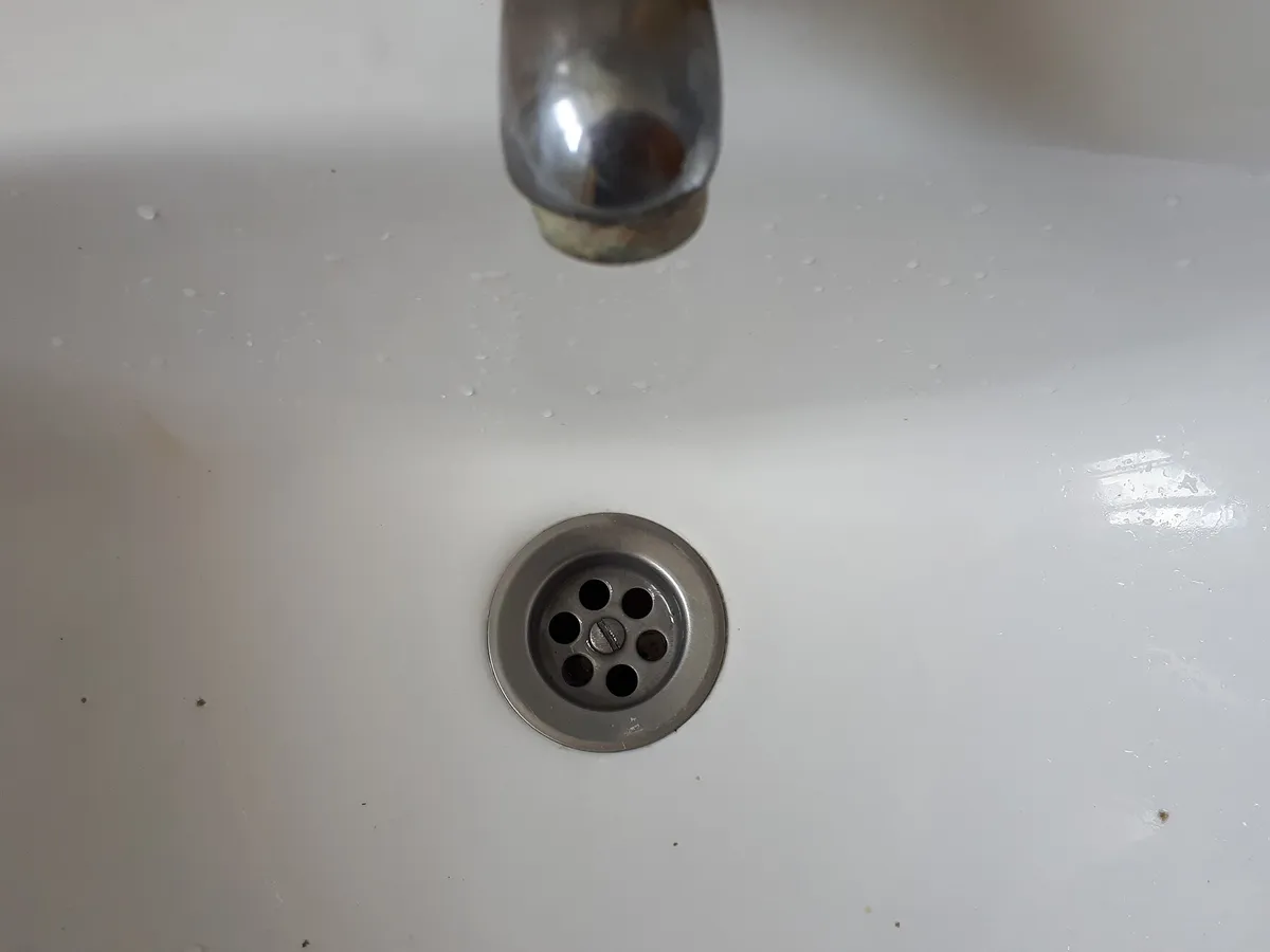 Bathroom sink with a chrome drain cover under a running faucet