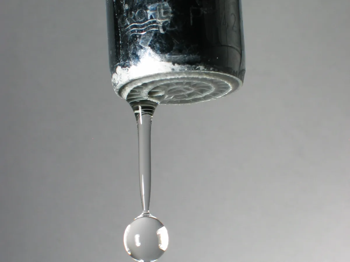 Close-up of a chrome faucet spout with a water drop forming at the tip